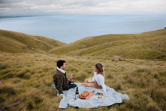 Image of two people drinking wine on a hill overlooking the ocean.